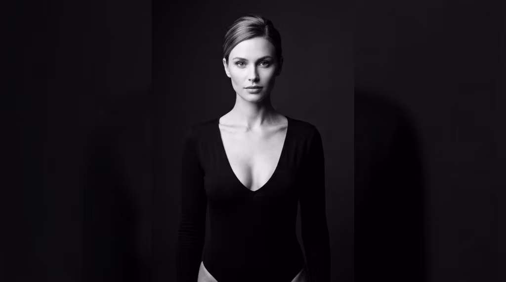Portrait en studio, en noir et blanc, d'une femme à l'expression assurée, vêtue d'un body noir à manches longues sur fond sombre.