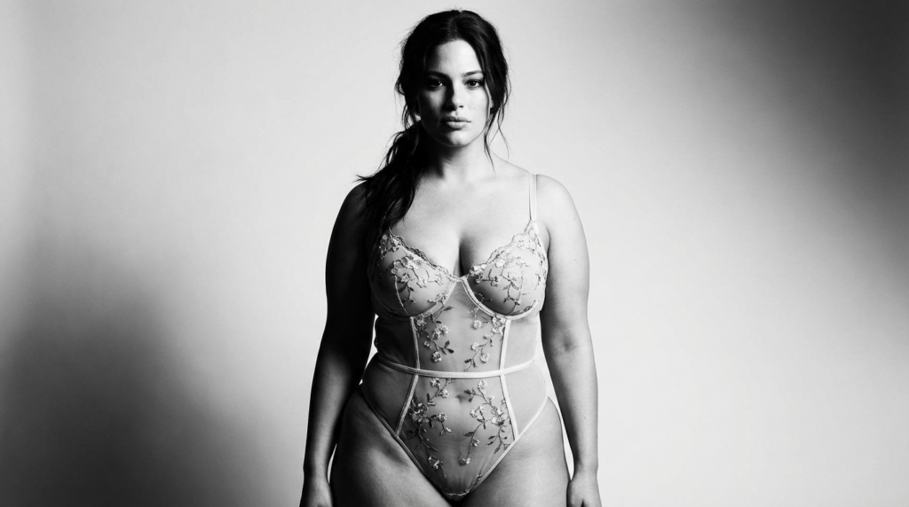 A black and white portrait of a confident woman with a natural look, wearing an elegant floral lace bodysuit.