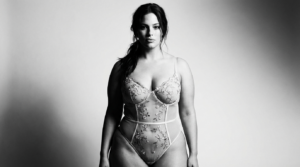 Ritratto in bianco e nero di una donna sicura di sé, dall'aspetto naturale, che indossa un elegante body in pizzo floreale.