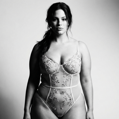 Ein Schwarz-Weiß-Porträt einer selbstbewussten Frau mit natürlichem Aussehen, die einen eleganten Body aus floraler Spitze trägt.