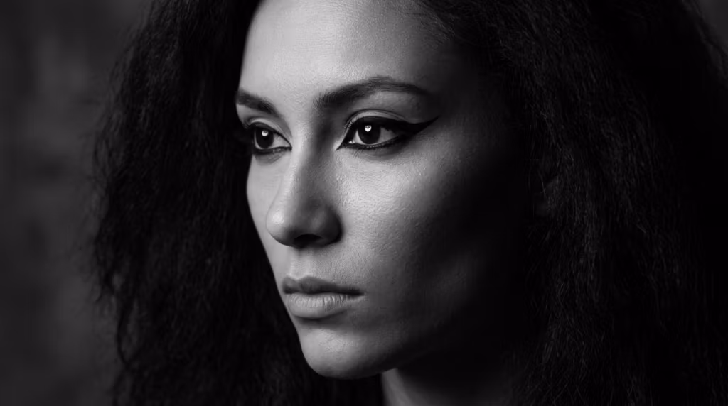 Een opvallend zwart-wit close-upportret van een vrouw met expressieve ogen en opvallende eyeliner, die peinzend opzij kijkt.
