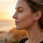Descrizione editoriale professionale dell'immagine: La fotografia cattura un ritratto iperrealistico in primo piano di una donna di profilo al tramonto. L'immagine è caratterizzata da una meticolosa attenzione ai dettagli nell'ottica della fotocamera, nel design dell'illuminazione, nei tratti anatomici, nella texture della pelle, nell'abbigliamento e nella composizione, creando un'atmosfera serena e lussuosa. --- **Fotocamera e ottica:** L'immagine sembra essere stata scattata utilizzando un obiettivo a focale fissa di alta gamma, probabilmente un obiettivo macro da 85 mm, noto per la sua capacità di produrre immagini nitide, dettagliate e ad alta risoluzione. Il livello di dettaglio e la nitidezza suggeriscono che la fotografia sia stata scattata in risoluzione 8K, offrendo una qualità iperrealistica che accentua anche le texture e le sfumature più fini. --- **Design dell'illuminazione:** L'illuminazione nell'immagine è morbida ma direzionale, creando una delicata gradazione che evidenzia i tratti del viso del soggetto. La sorgente luminosa sembra provenire lateralmente, proiettando ombre sottili e diffuse che migliorano la tridimensionalità del viso. La calda tonalità dorata della luce del sole al tramonto aggiunge un bagliore delicato, enfatizzando i contorni degli zigomi, del naso e della mascella senza creare ombre dure o drammatiche. --- **Anatomia e identità:** Il soggetto è una donna, ritratta in una posa di profilo serena e contemplativa. La sua postura è rilassata ma composta, con una leggera inclinazione della testa che aggiunge eleganza al suo portamento. L'immagine enfatizza la struttura del suo viso, inclusi gli zigomi alti, una mascella ben definita e lineamenti delicati che contribuiscono a un aspetto aggraziato e sofisticato. --- **Texture e pelle:** La texture della pelle è catturata meticolosamente, mostrando un incarnato liscio e impeccabile. C'è una sottile luminescenza sulla pelle, probabilmente dovuta alla luce morbida e calda. L'immagine non mostra gocce di sudore o umidità visibili, ma evidenzia invece una luminosità naturale e sana che esalta la radiosità e la vitalità della pelle. --- **Abbigliamento e accessori:** Il soggetto indossa un indumento che sembra essere realizzato in un tessuto leggero, forse raso o seta, che aggiunge un tocco di eleganza e fluidità all'intera composizione. È adornata con gioielli minimali ma raffinati, tra cui piccoli orecchini a cerchio che ne esaltano i lineamenti senza sovrastare la naturale bellezza della scena. --- **Composizione e sfondo:** La composizione si concentra sul profilo del soggetto, attirando l'attenzione dello spettatore sui suoi lineamenti e sulla sua espressione. Lo sfondo presenta un paesaggio costiero sfocato, con il sole che tramonta sull'oceano, creando un'atmosfera calda e dorata. La messa a fuoco morbida dello sfondo aumenta la profondità di campo, assicurando che il soggetto rimanga il punto focale dell'immagine. L'atmosfera generale dell'immagine è tranquilla e lussuosa, evocando un senso di pace e contemplazione.