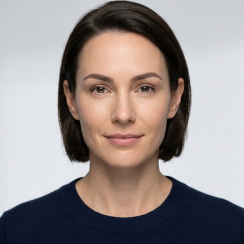 This high-resolution editorial portrait captures a woman with a serene expression, rendered with the precision of professional DSLR photography. Shot with a sharp, medium-telephoto lens—likely an 85mm—the image prioritizes subject clarity, isolating the subject from a clean, minimalist studio background. The lighting is soft and diffused, creating a flattering, even illumination across the face that minimizes harsh shadows while accentuating the natural, healthy skin texture and balanced facial features. The subject’s skin exhibits a natural, matte-like finish with lifelike micro-details, emphasizing a polished and professional aesthetic. She is wearing a minimalist, dark navy blue knit sweater with a fine-gauge texture, providing a subtle contrast against the high-key, neutral backdrop. The composition is a classic, centered head-and-shoulders portrait, conveying a sense of sophistication, accessibility, and calm confidence.
