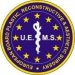 Kreisförmiges Logo des European Board of Plastic, Reconstructive & Aesthetic Surgery (UEMS) mit blauem Hintergrund, gelben Sternen und einem weißen medizinischen Symbol in der Mitte.