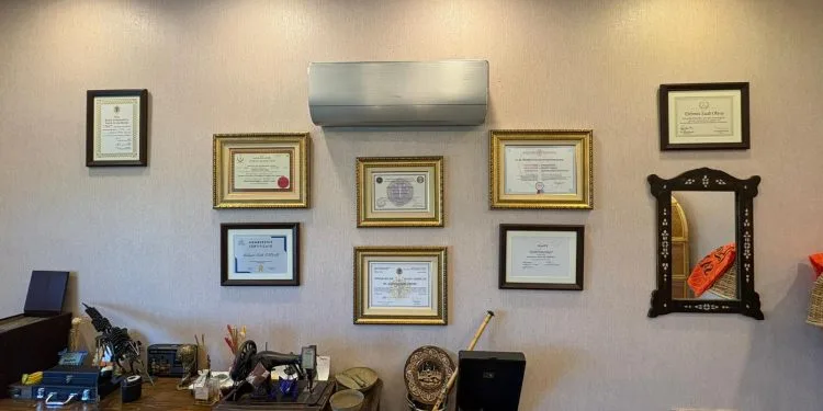 Pared decorada con diversos certificados médicos, diplomas y un espejo en un entorno clínico profesional.