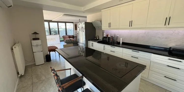 Moderna cocina de clínica con isla de granito negro, armarios blancos y una sala de espera al fondo en la clínica del Dr. MFO.