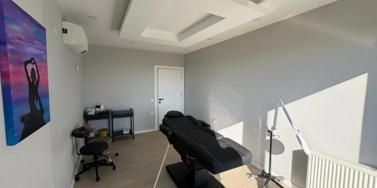 Una sala de tratamiento de una clínica de medicina estética limpia y moderna, equipada con una camilla ajustable de color negro, un taburete con ruedas, una lámpara profesional y obras de arte decorativas en la pared.