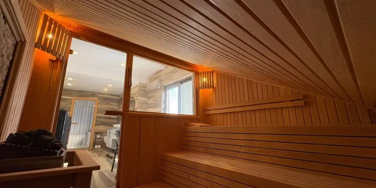 Interior de sauna moderna de madera con iluminación cálida y una puerta de cristal que da a un baño en una clínica de bienestar.