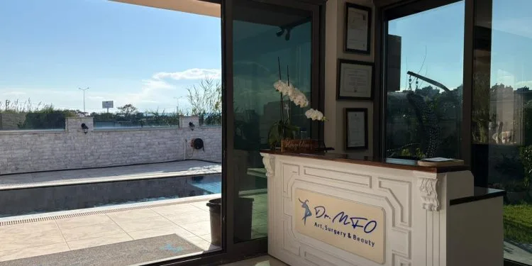 Mostrador de recepción de la clínica de arte, cirugía y belleza del Dr. MFO, con vistas a una piscina exterior y una terraza.